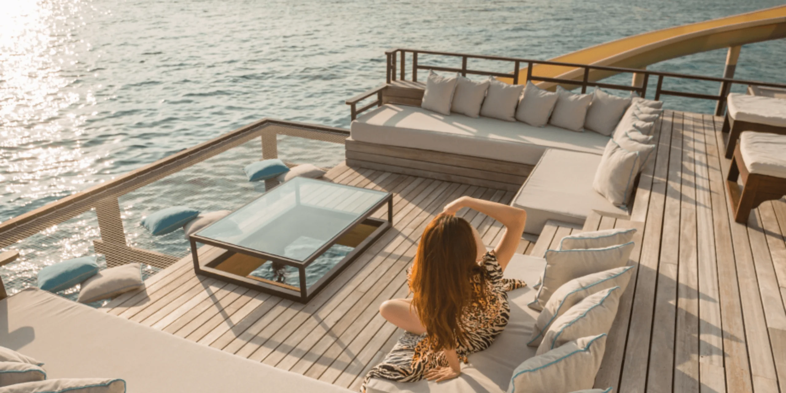 Woman sitting on deck above ocean with lounge seating