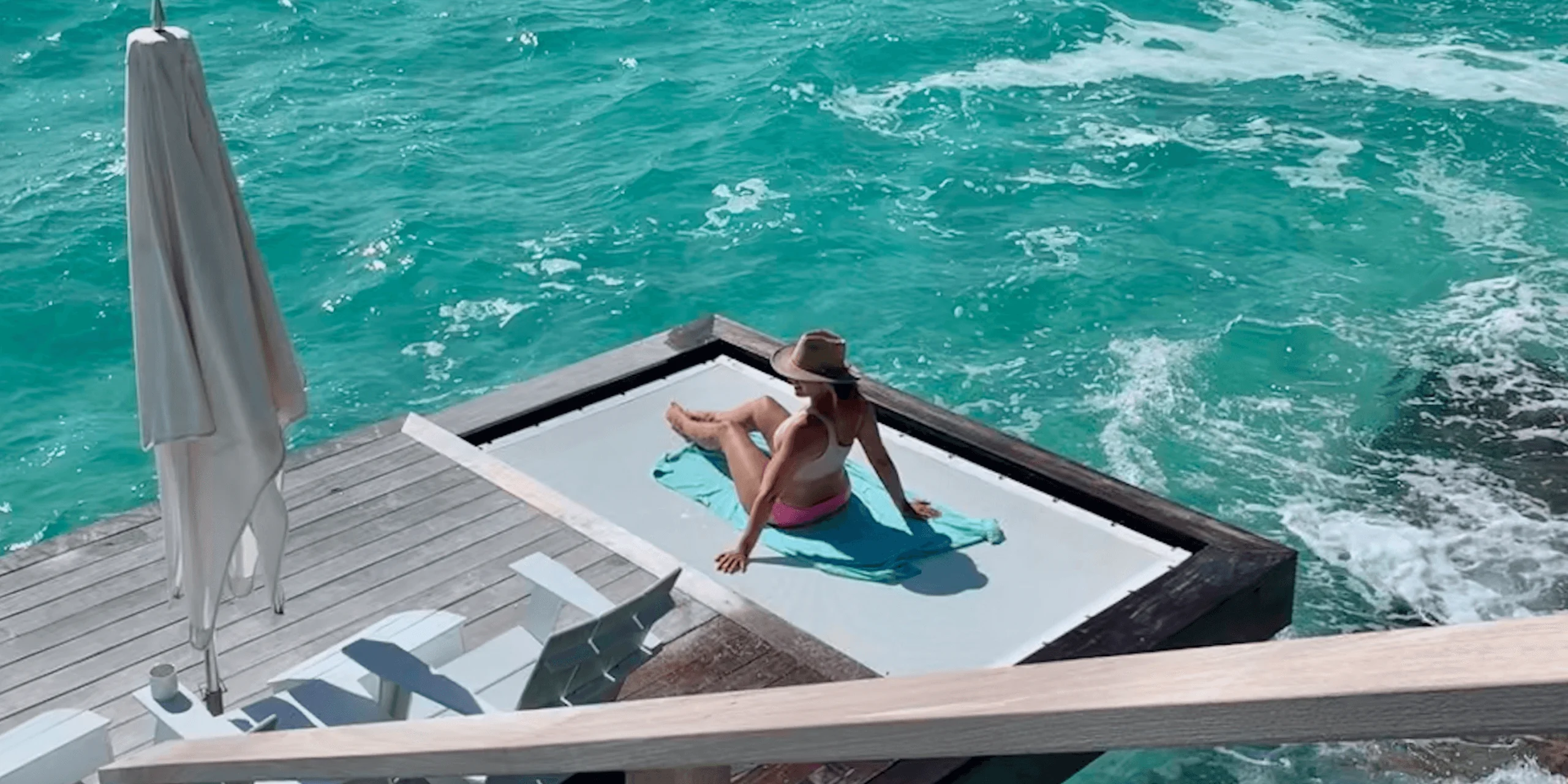 Woman relaxing on platform above clear turquoise water