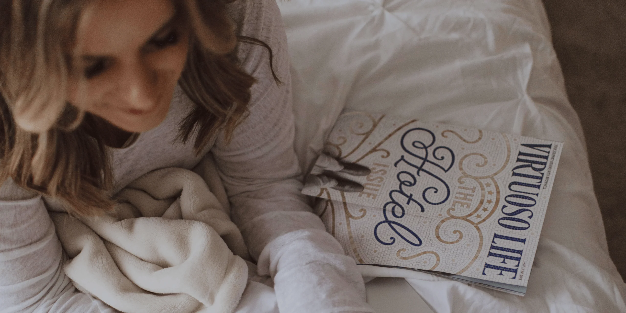 Woman reading Virtuoso Life magazine in bed