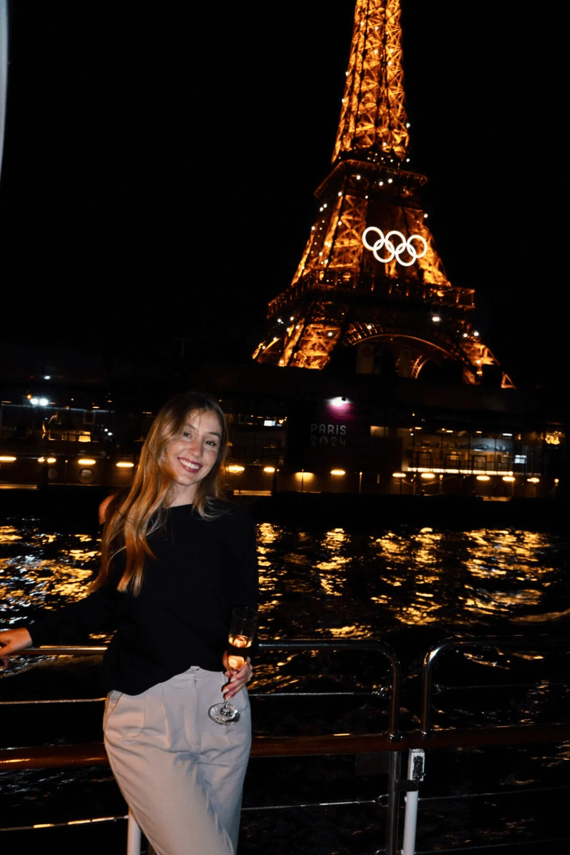 Woman standing on a boat on the Seine River with the Eiffel Tower illuminated at night in Paris
