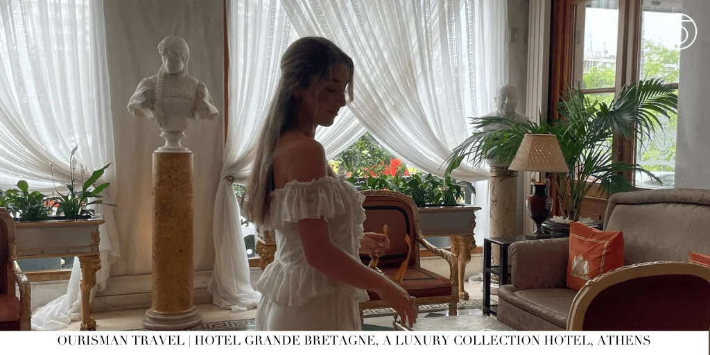 Guest standing in an elegant lounge at Hotel Grande Bretagne in Athens with classical statues and draped windows