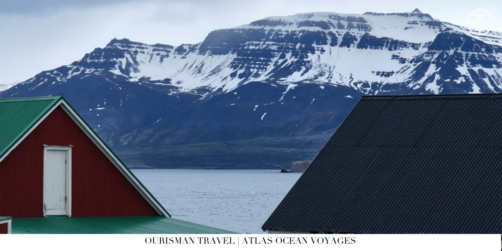 Red coastal house with snow-capped mountains overlooking a fjord in Iceland