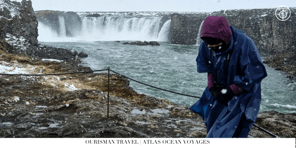 Traveler in rain gear standing near a powerful waterfall in Iceland