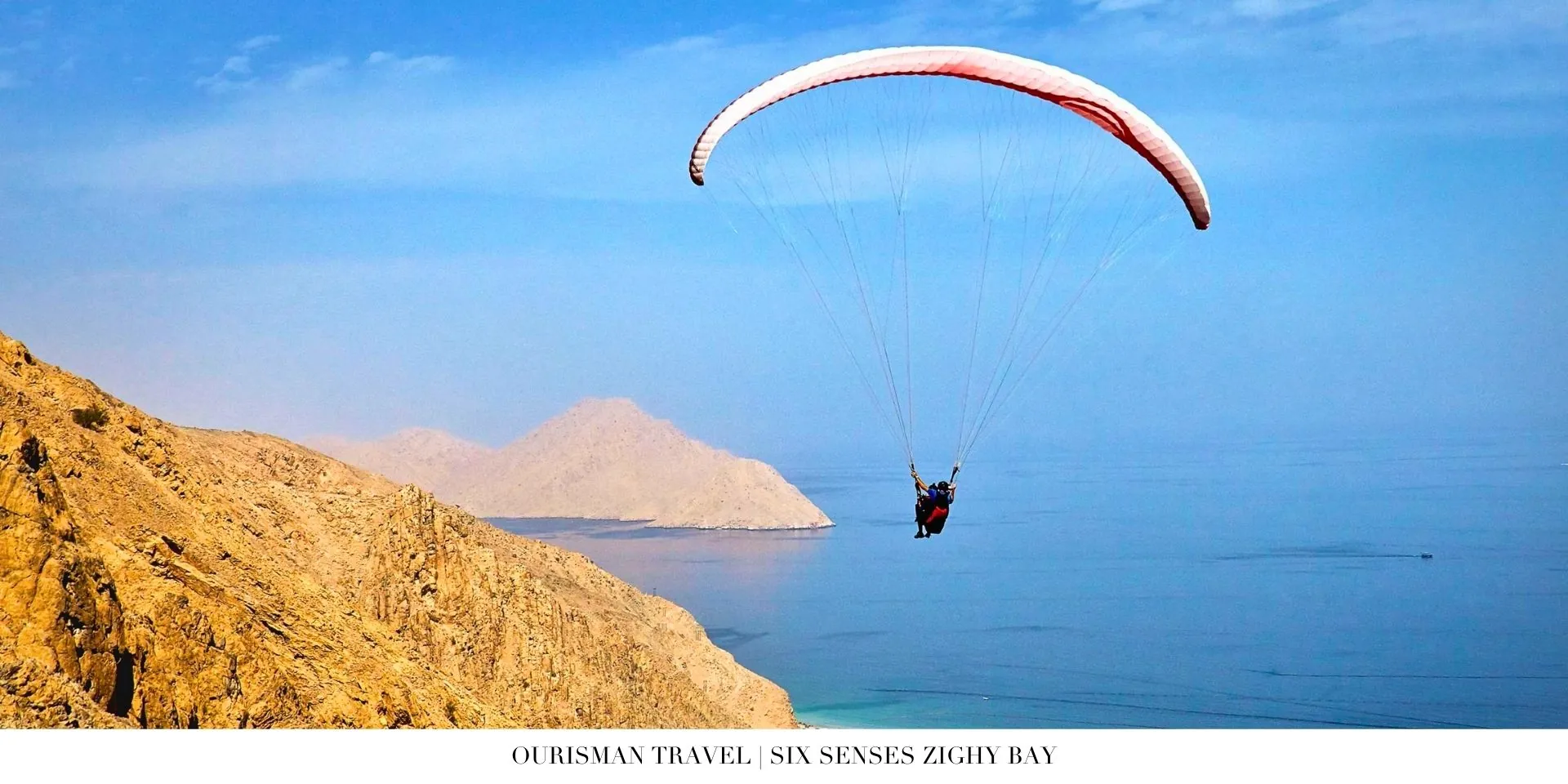 Paragliding arrival experience above Six Senses Zighy Bay with dramatic mountain backdrop